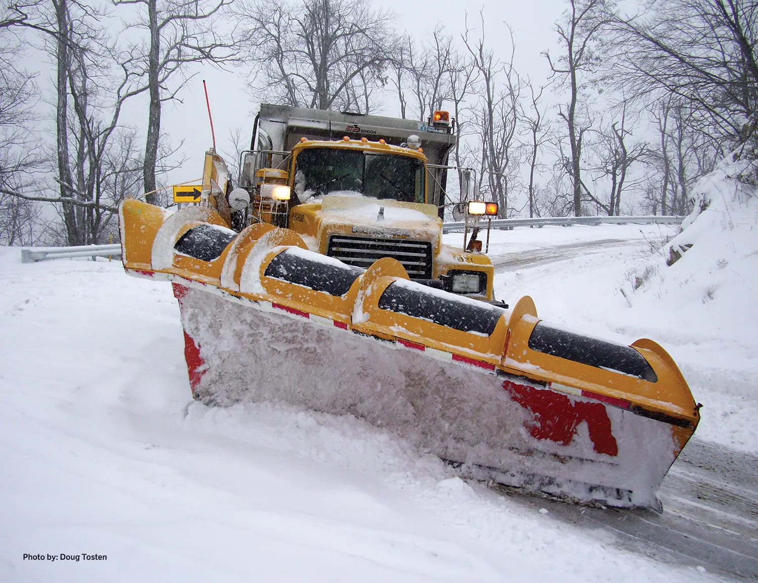A snow plow truck pushes snow off a roadway curve.